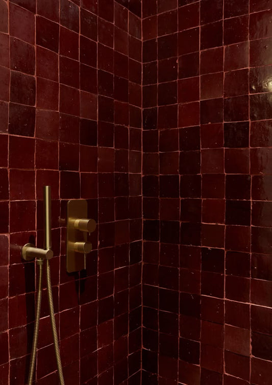 Handmade Moroccan Zellige tile in deep burgundy red glaze installed in modern shower with brass fixtures