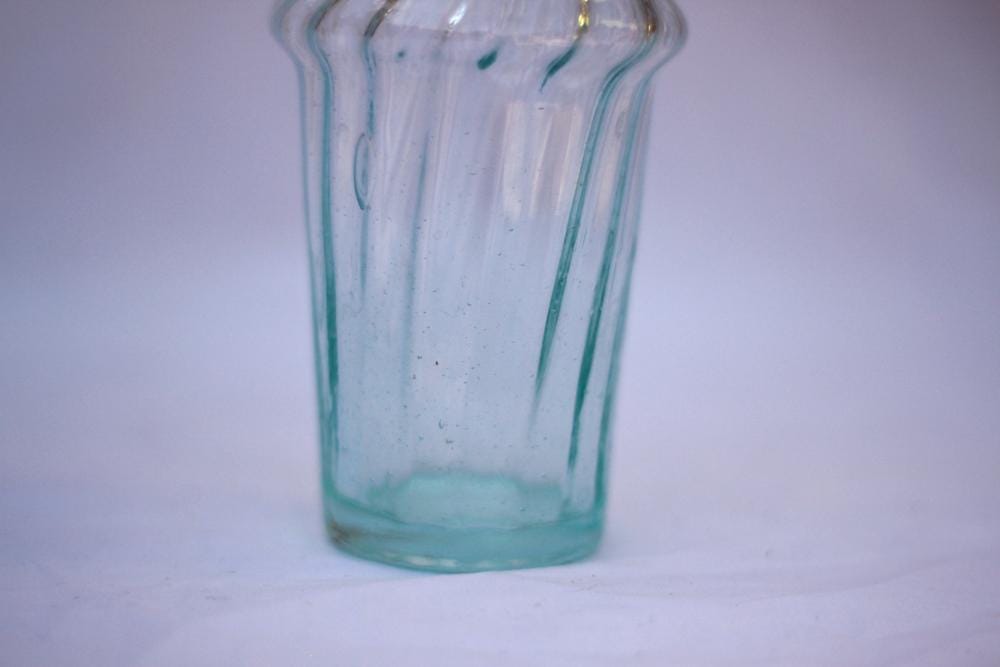 Close-up of a clear fluted glass vessel against a plain white background, House of Anouar