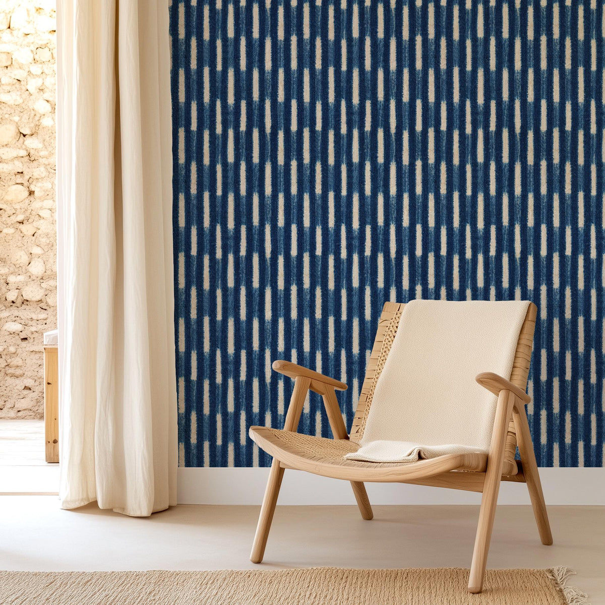 Indigo Baule strip-weave wallpaper behind a wooden lounge chair, House of Anouar