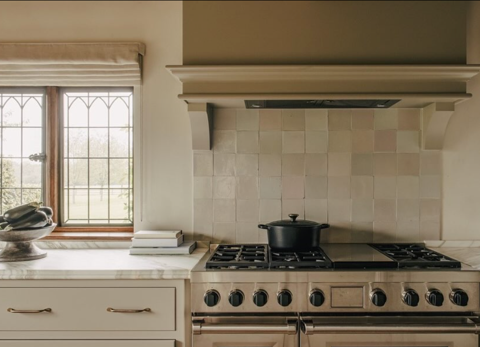 Handmade neutral Moroccan Zellige tiles in 4x4 inches 2x2 inches 10x10 cm and 5x5 cm installed as a backsplash behind a classic range in a traditional kitchen with marble countertops and arched hood